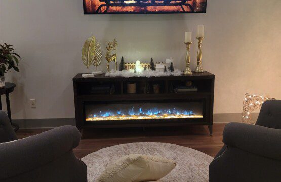 Electric fireplace glowing with blue flames amid gold holiday accents and candlelight in the living room