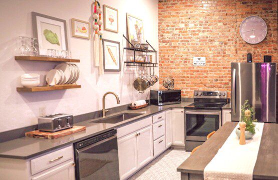 Full kitchen with exposed brick, quartz counters, stainless appliances, and open shelving