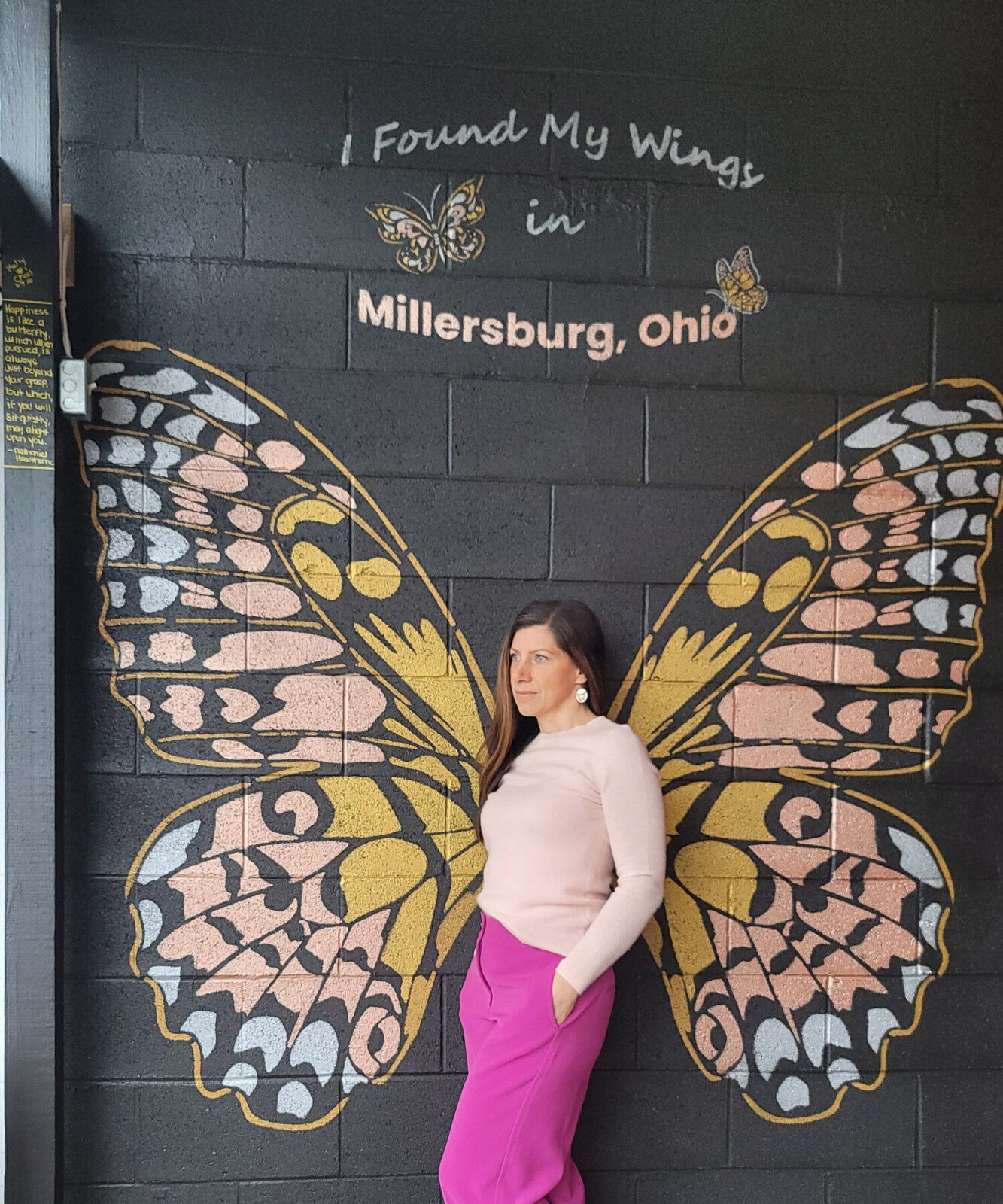 Owner- Kelly posing before the hand-painted butterfly mural with sweeping gold and pastel wings at Suite on Jackson
