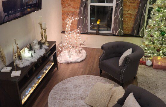 Living area decked for Christmas with lit twig trees, garland, and a decorated tree by the electric fireplace