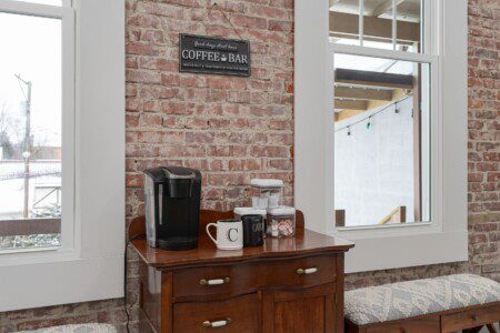 Coffee bar with a Keurig, mugs, and signage on an antique buffet against exposed brick