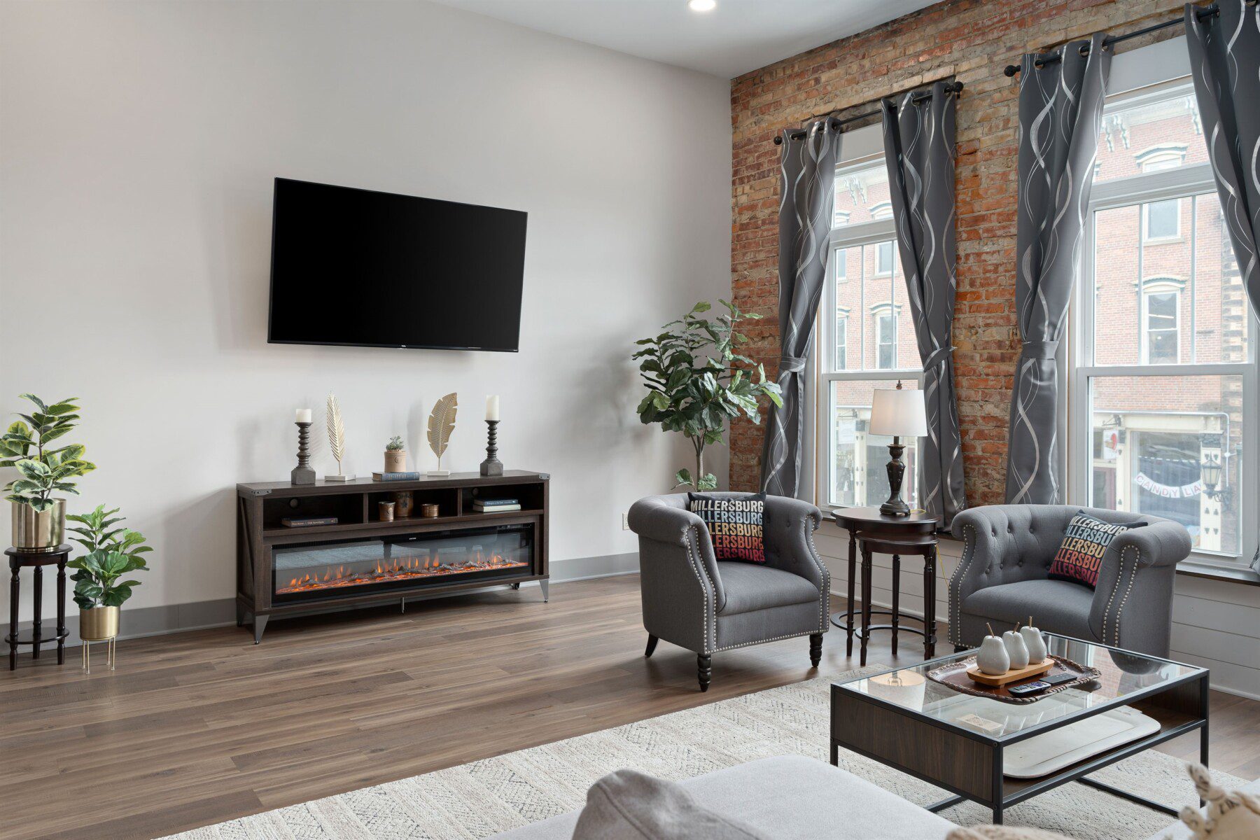 Living room with a wall-mounted TV, electric fireplace, and tufted chairs by windows overlooking Millersburg