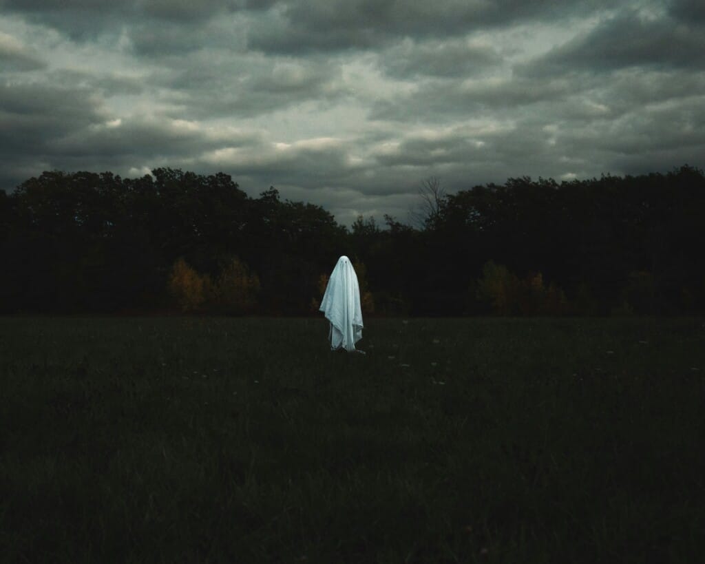 A lone ghostly figure draped in white stands in a dark, misty Ohio field at dusk