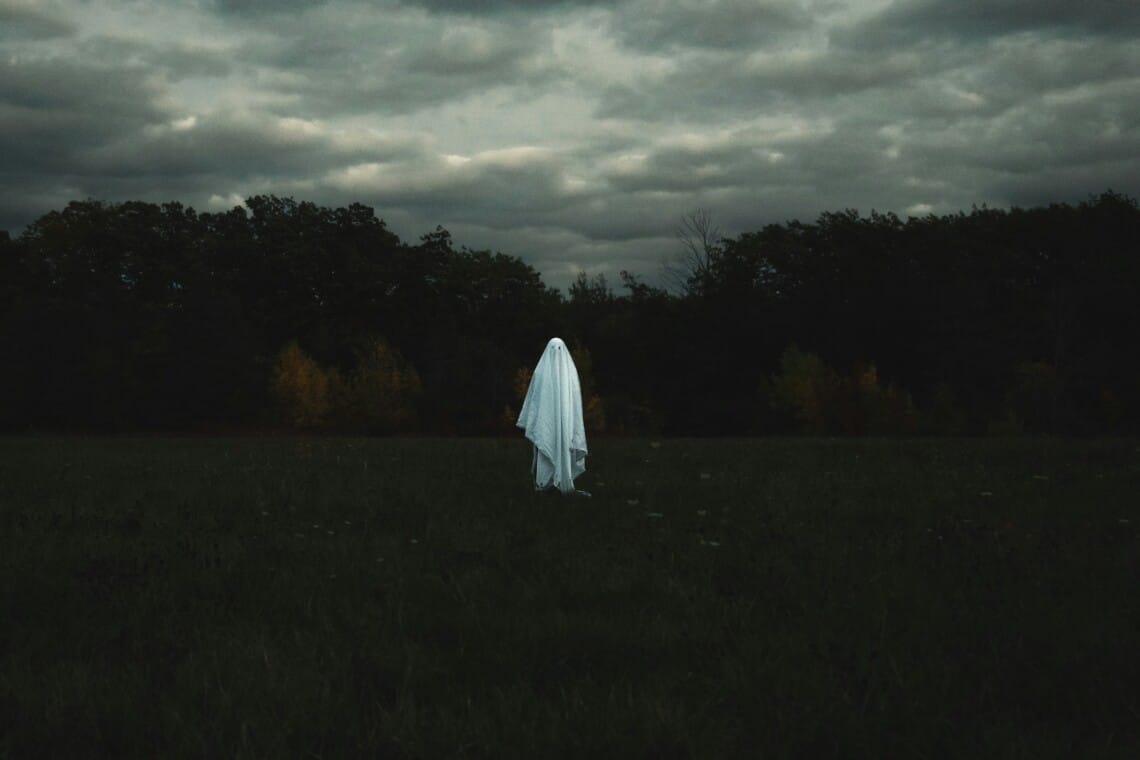 A lone ghostly figure draped in white stands in a dark, misty Ohio field at dusk